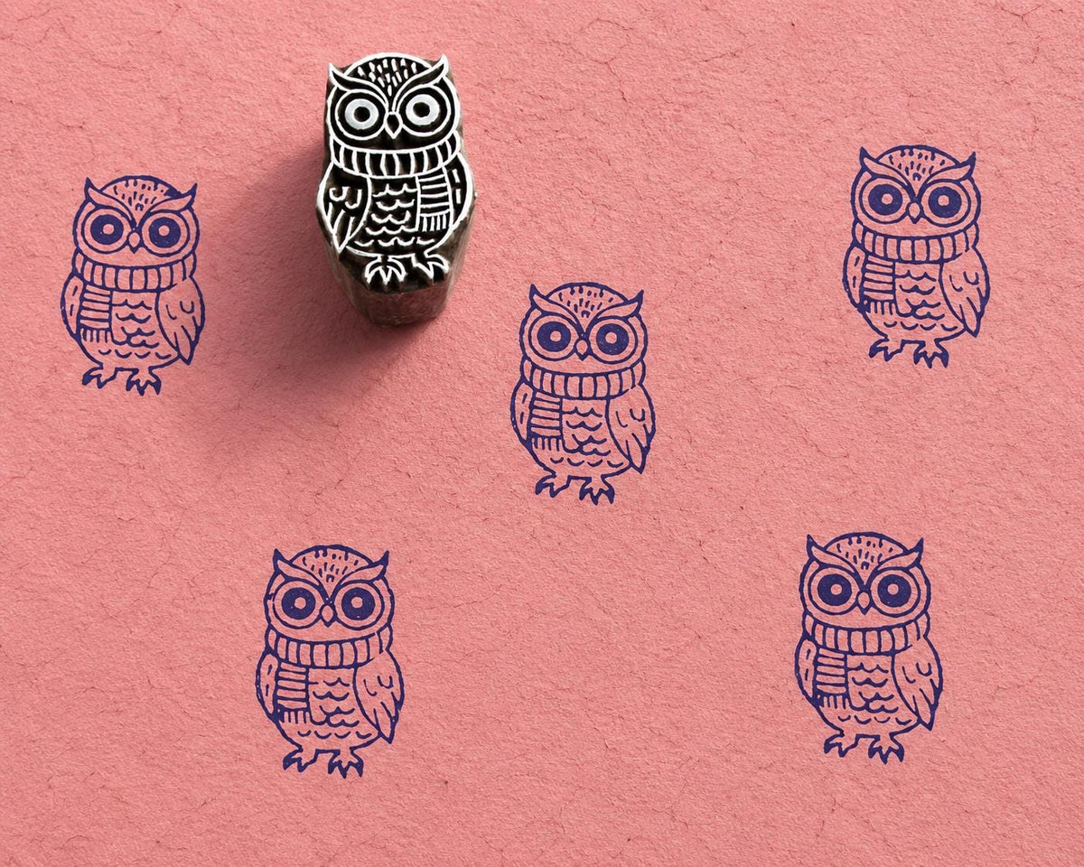 Hand carved wooden owl block stamp with winter scarf design and blue impressions on textured pink handmade paper