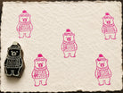 Hand carved Winter Bear wooden block stamp with bright pink impressions on handmade paper.