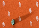 Tiny hand carved wooden leaf sprig block stamp printing delicate repeating botanical motif in white ink on textured terracotta paper
