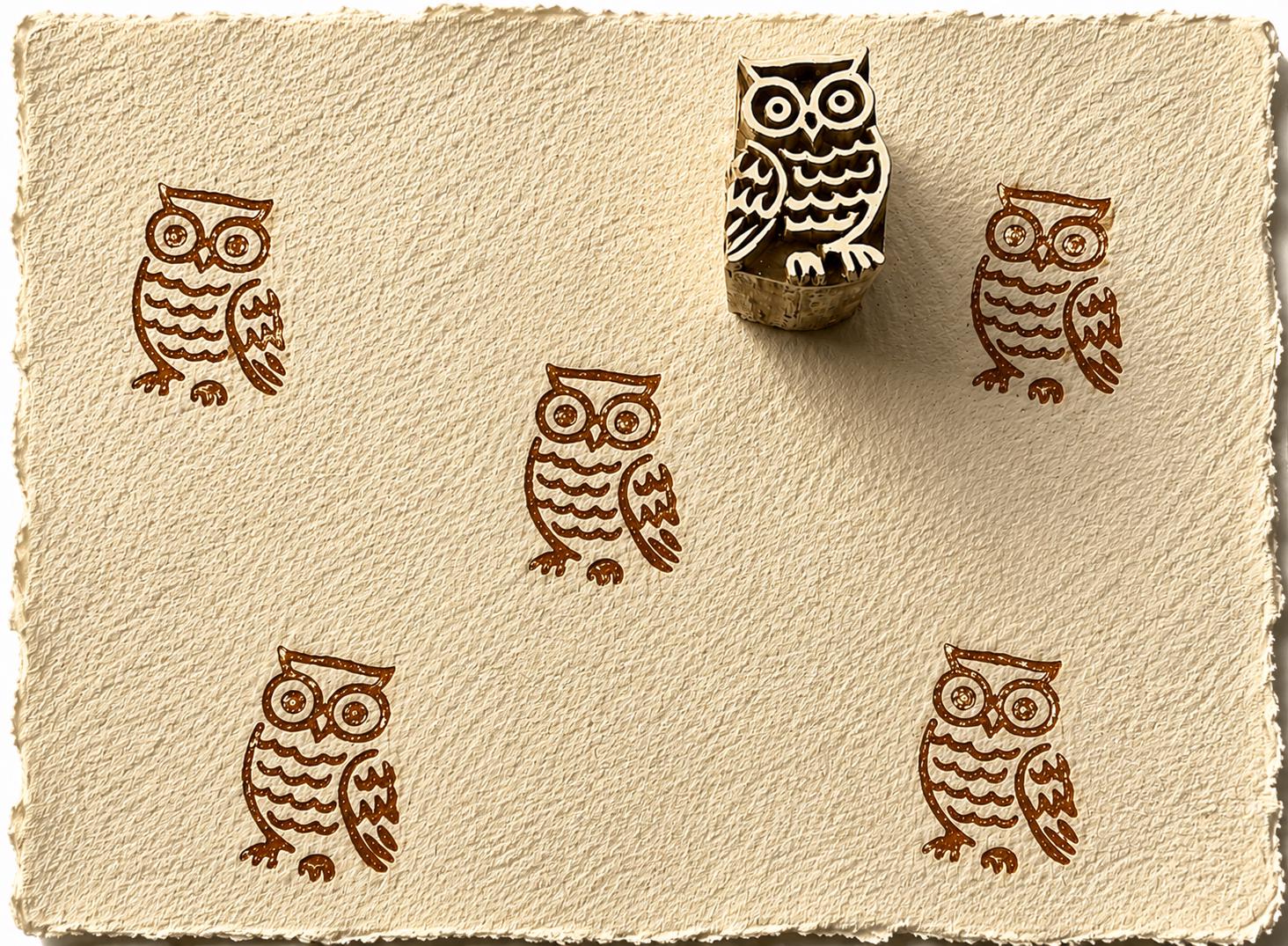 Hand carved owl block stamp creating repeated owl impressions on handmade paper.