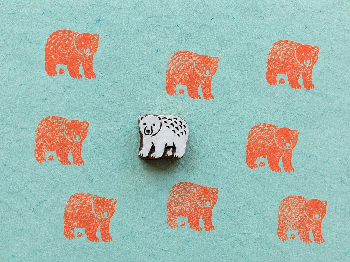 Hand carved bear stamp producing repeated wildlife pattern prints on textured paper.