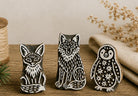 Hand carved wooden printing block set featuring fox wolf and penguin stamps displayed on a rustic craft table.