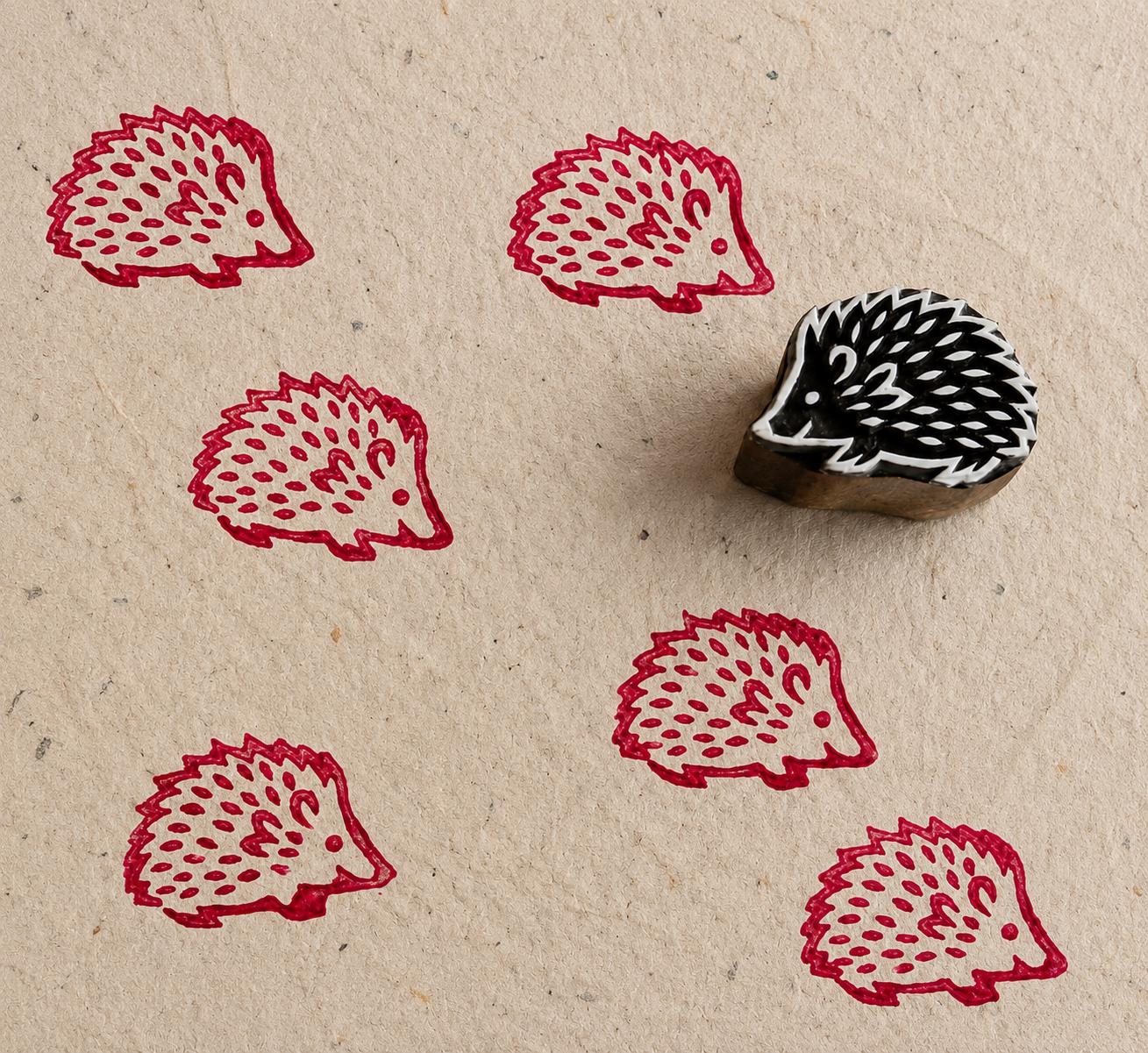 Hand carved hedgehog wood block stamp printing repeating folk animal patterns on textured paper