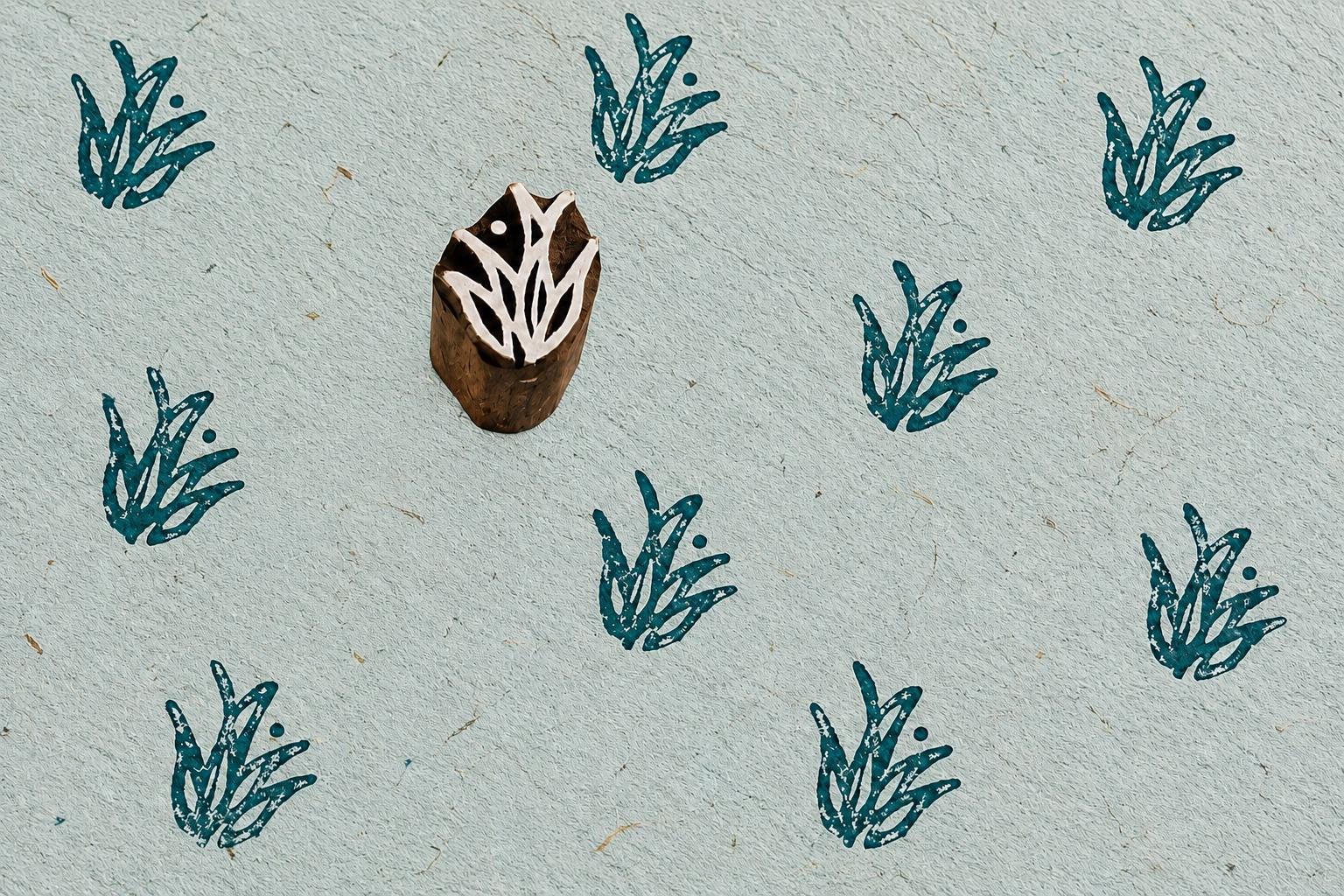 Hand carved wild grass sprig stamp creating repeated botanical impressions on handmade textured paper.