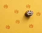 Hand carved storybook crown stamp creating repeated crown motif impressions on handmade textured paper.