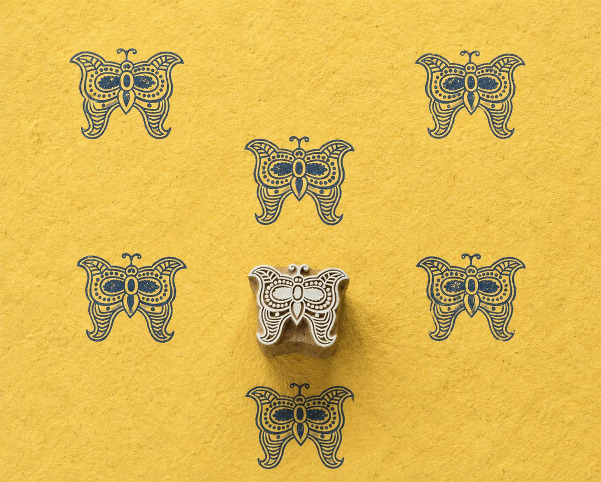 Hand carved Folk Butterfly wooden block stamp with navy blue impressions on yellow handmade paper.