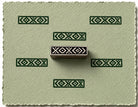 Hand carved wooden border printing block featuring a repeating diamond and chevron pattern stamped in green on textured handmade paper.
