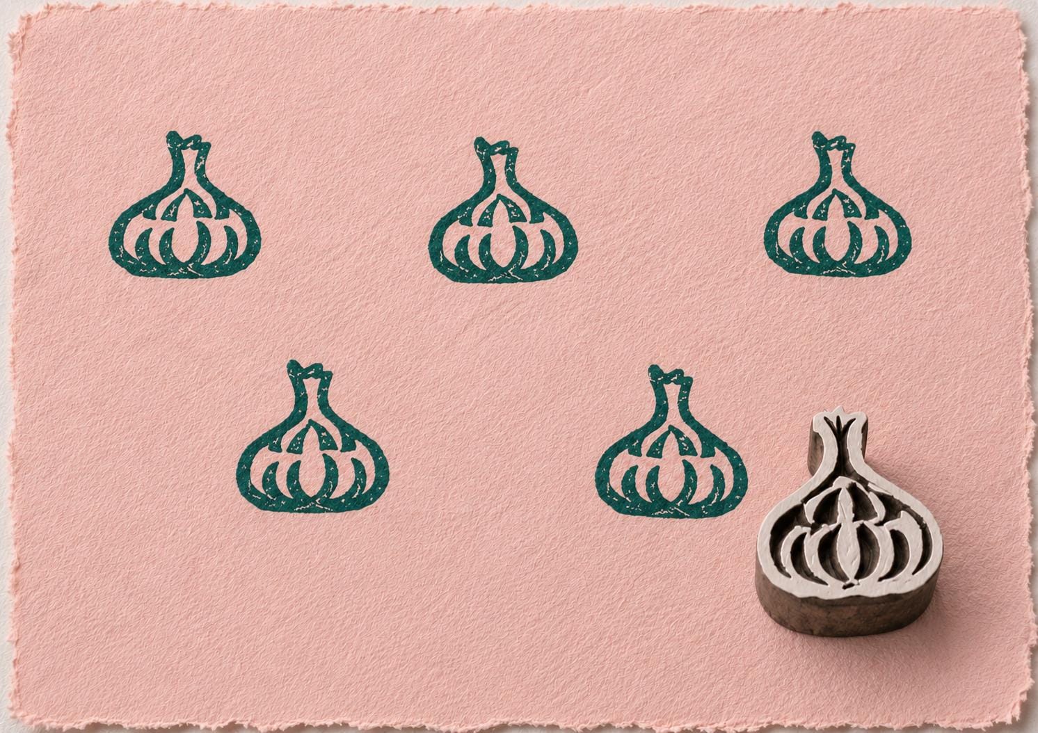 Hand carved Indian wooden printing block featuring a garlic bulb motif stamped in deep teal on blush pink handmade paper, suitable for fabric printing, pottery decoration, clay impressions, and kitchen-inspired crafts.