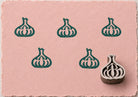 Hand carved Indian wooden printing block featuring a garlic bulb motif stamped in deep teal on blush pink handmade paper, suitable for fabric printing, pottery decoration, clay impressions, and kitchen-inspired crafts.