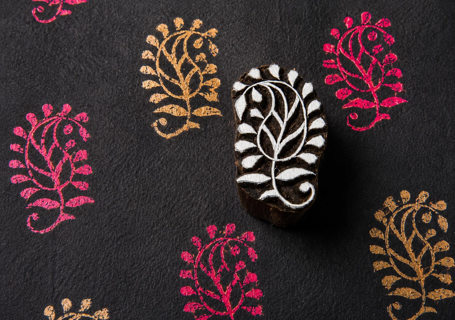 Hand carved Paisley Bloom wooden block stamp with folk paisley prints in gold and magenta on black handmade paper.