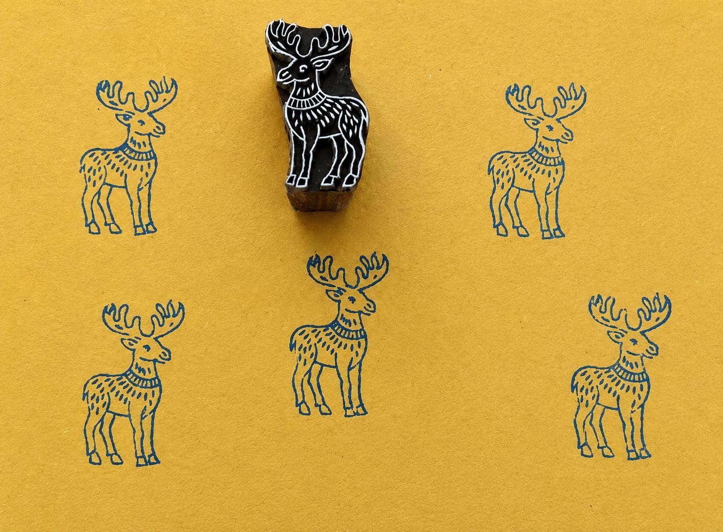 Hand carved moose block stamp creating a repeating folk animal pattern on handmade paper