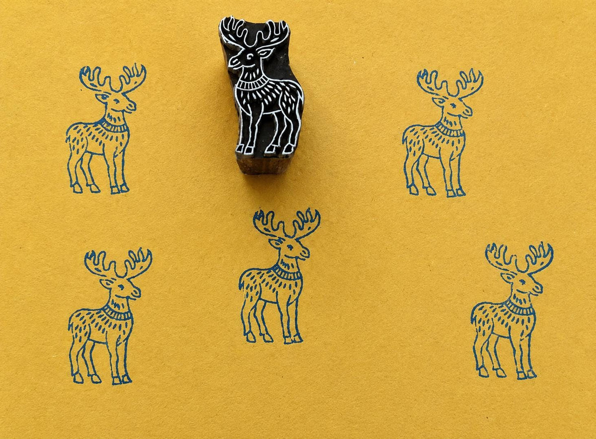 Hand carved moose block stamp creating a repeating folk animal pattern on handmade paper