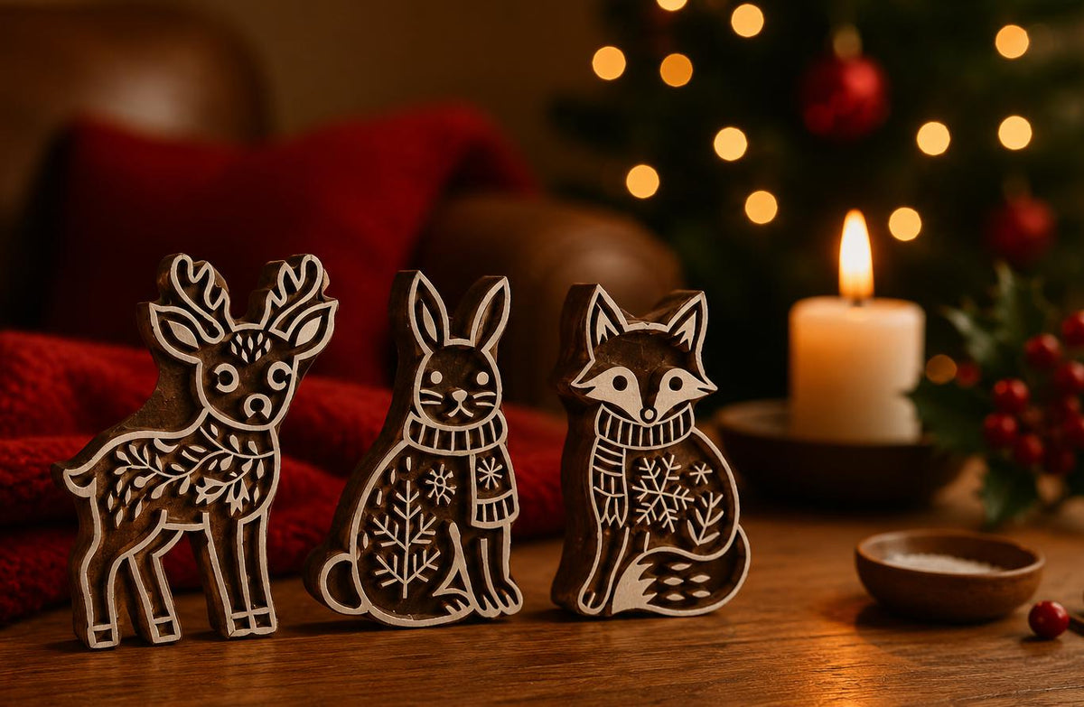 Three hand carved wooden printing blocks featuring a winter deer, rabbit and fox displayed in a cozy Christmas setting with candlelight.