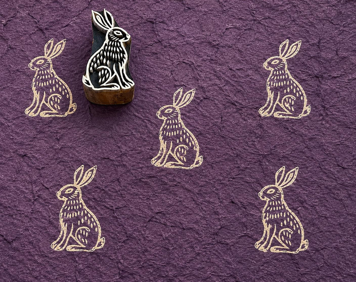 Hand carved Woodland Hare wooden block stamp with ivory impressions on textured plum handmade paper.