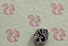 Hand-carved wooden printing block featuring a squirrel holding an acorn, stamped in berry pink ink on textured handmade paper.