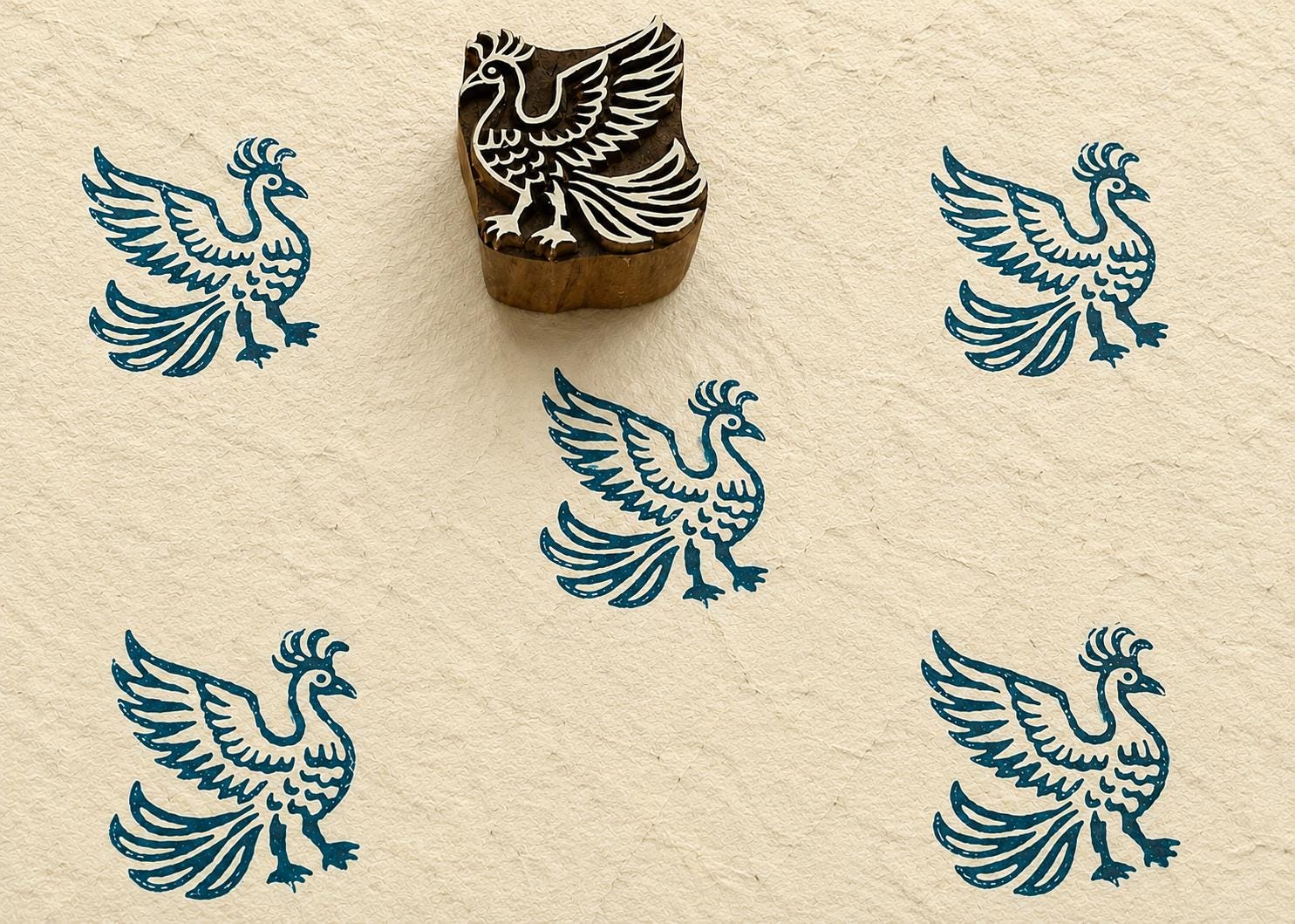 Hand-carved wooden printing block featuring a stylized phoenix bird with raised wings and flowing tail feathers, stamped in teal ink on handmade paper.