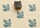 Hand-carved wooden printing block featuring a stylized phoenix bird with raised wings and flowing tail feathers, stamped in teal ink on handmade paper.
