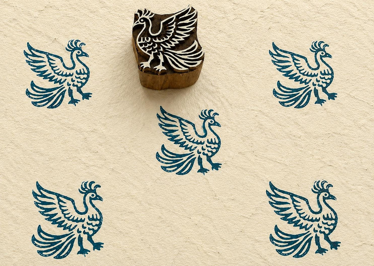 Hand-carved wooden printing block featuring a stylized phoenix bird with raised wings and flowing tail feathers, stamped in teal ink on handmade paper.