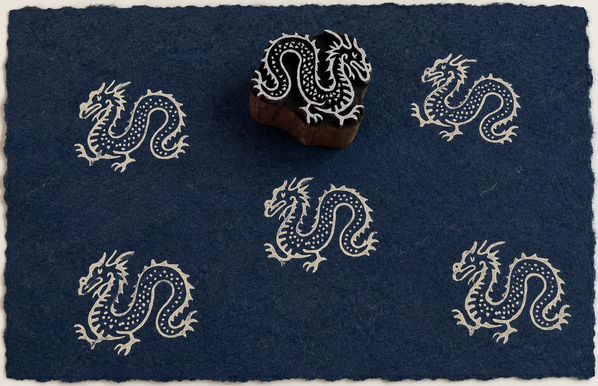 Hand carved Celestial Dragon wooden block stamp with ivory impressions on deep indigo handmade paper.