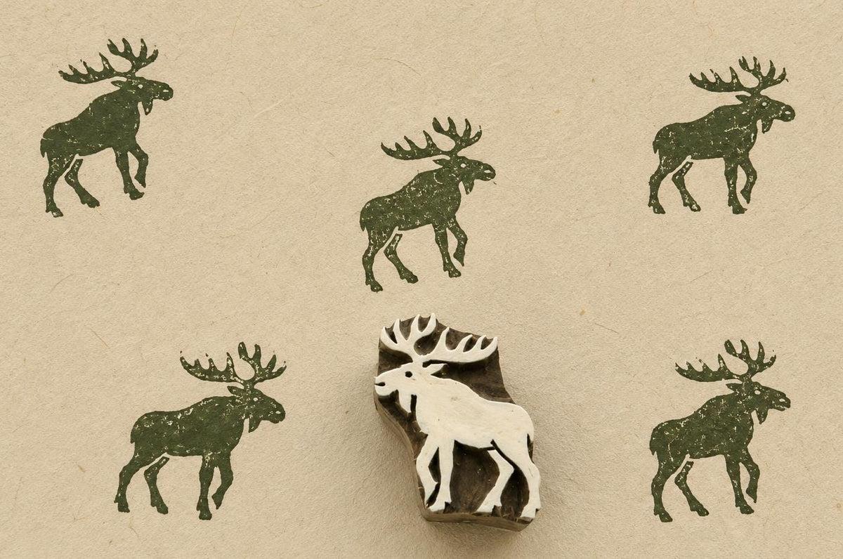 Hand carved Indian wooden printing block featuring a Nordic moose silhouette stamped in forest green on handmade paper, suitable for fabric printing, pottery decoration, clay impressions, and woodland craft projects.