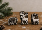 Collection of hand carved wooden printing blocks featuring a bear, stag and moose displayed on a rustic wooden table with woodland-inspired styling.