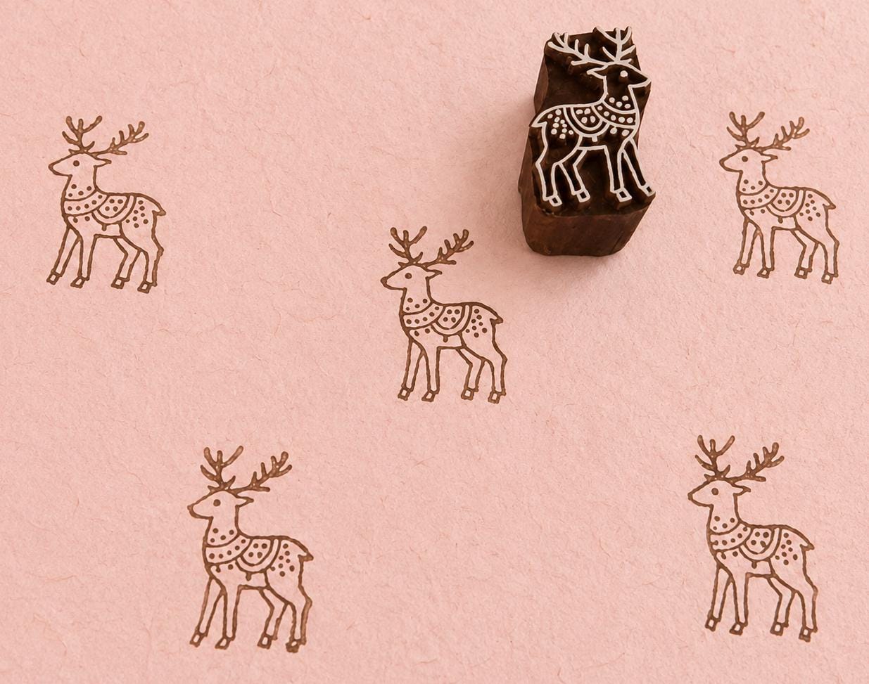 Hand carved Woodland Herald Deer wooden block stamp with decorative deer impressions on soft pink handmade paper.