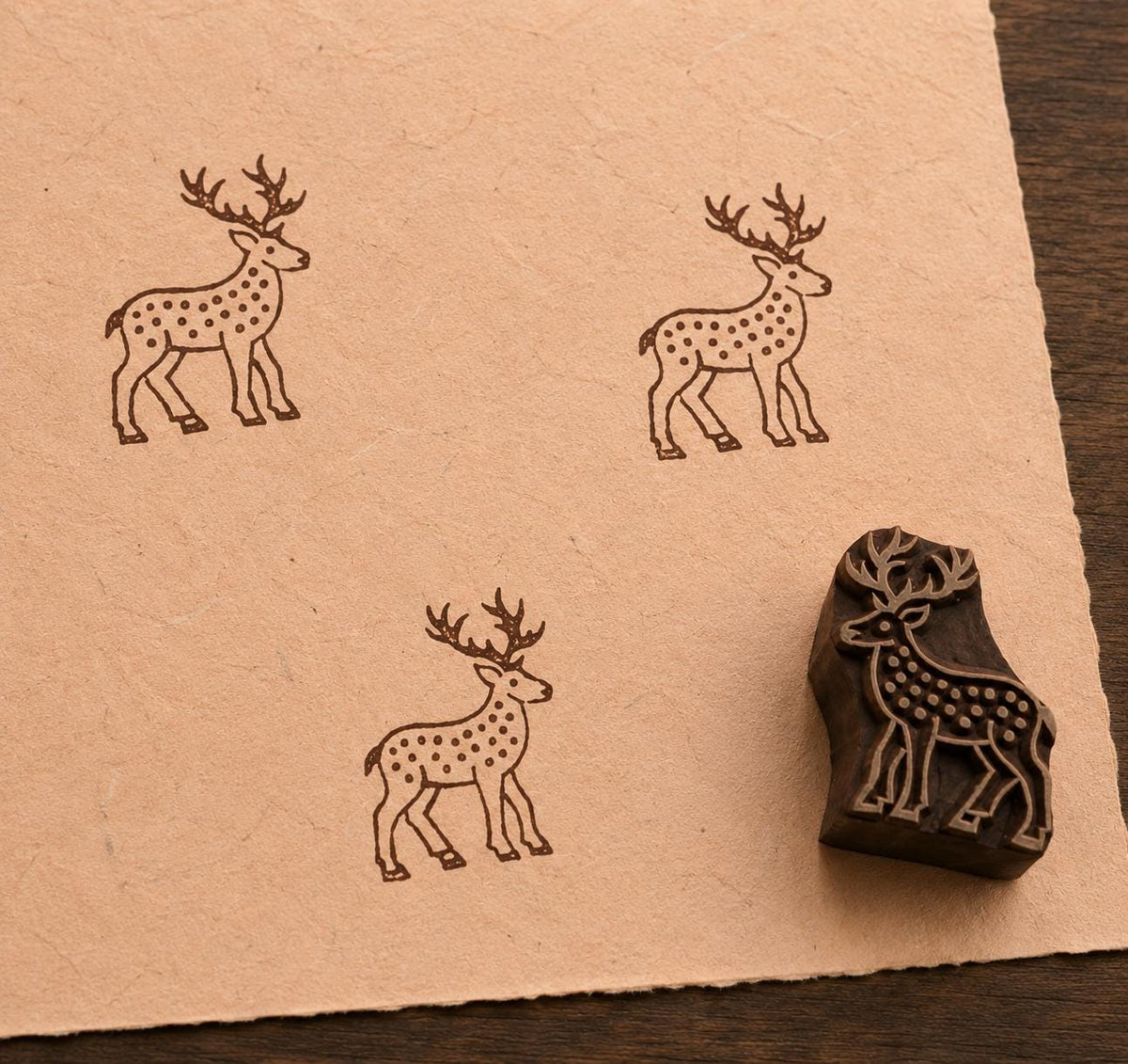 Hand carved spotted deer wooden printing block with repeated deer impressions on handmade paper
