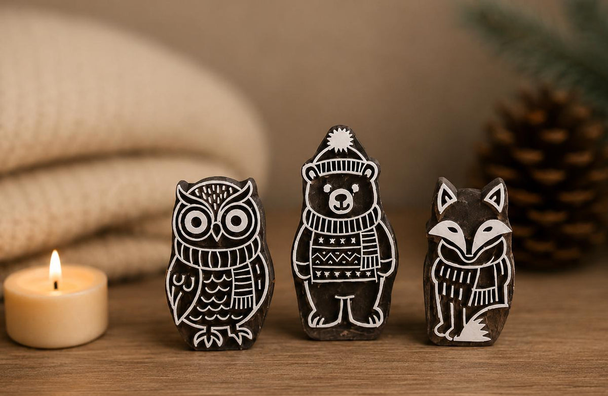 Set of three winter woodland wooden printing blocks featuring an owl, bear and fox displayed on a rustic tabletop