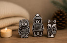 Set of three winter woodland wooden printing blocks featuring an owl, bear and fox displayed on a rustic tabletop