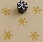 Hand carved snowflake wooden printing block with repeated golden snowflake impressions on handmade paper