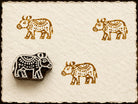 Hand-carved wooden printing block stamp featuring a decorative folk cattle design with ornamental patterns, shown stamped in ochre ink on handmade paper.