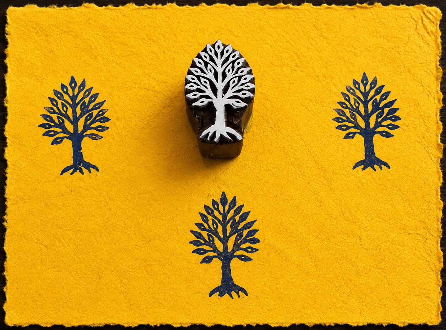 Hand carved Sacred Tree wooden block stamp with blue impressions on handmade yellow paper.