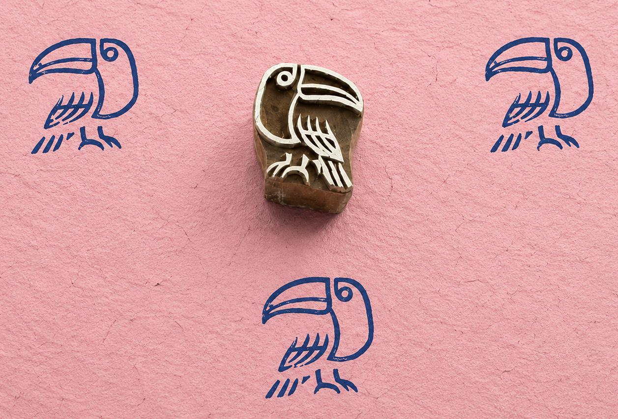 Hand carved folk art toucan block stamp with blue tropical bird impressions on pink handmade paper