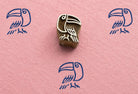 Hand carved folk art toucan block stamp with blue tropical bird impressions on pink handmade paper