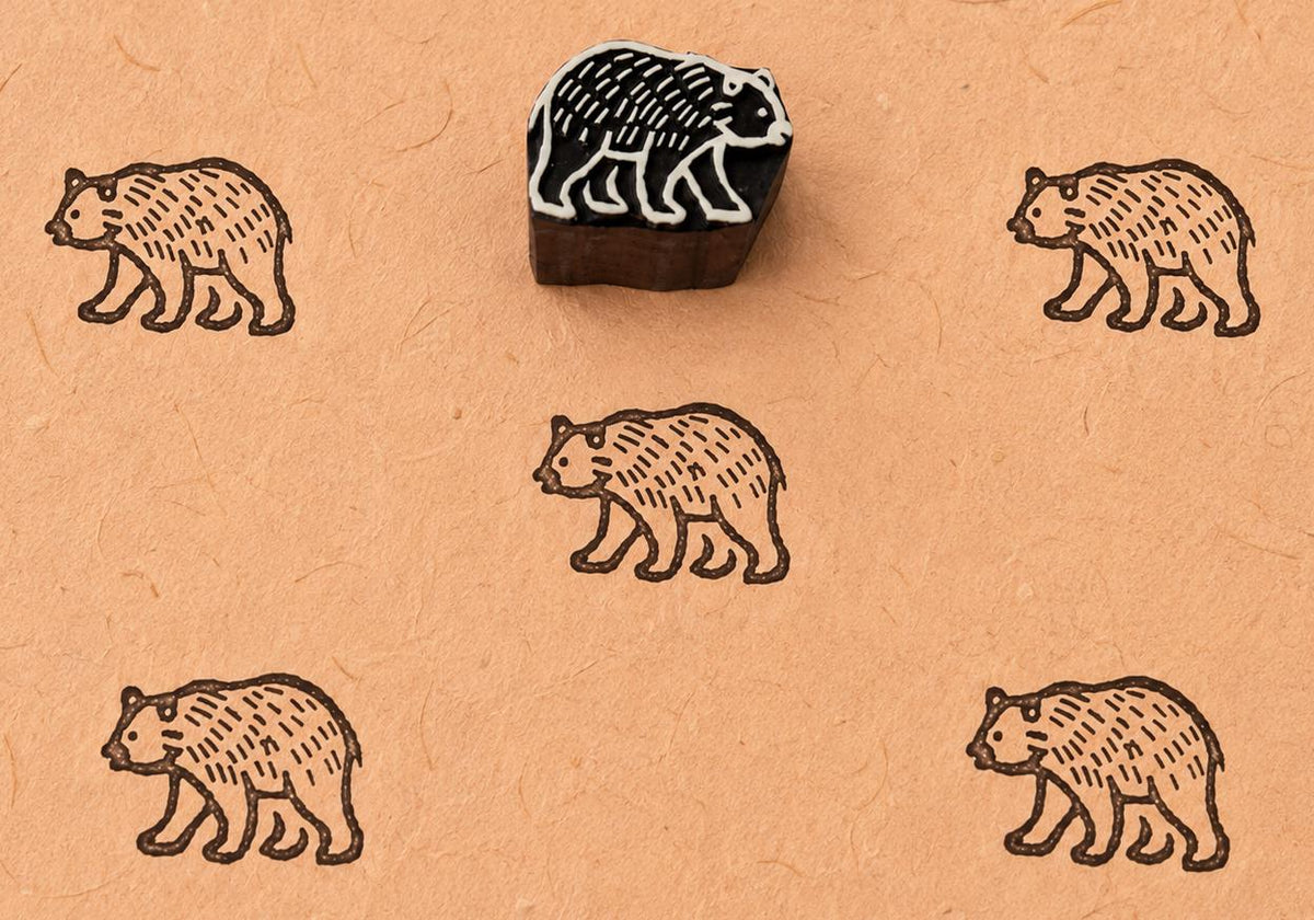 Hand carved Wandering Bear wooden block stamp with brown bear impressions on handmade paper.