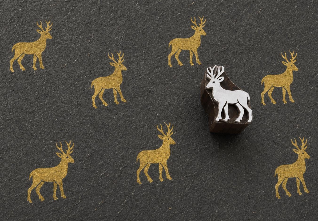 Hand-carved wooden printing block featuring a standing buck deer with branching antlers stamped in metallic gold on textured black handmade paper.