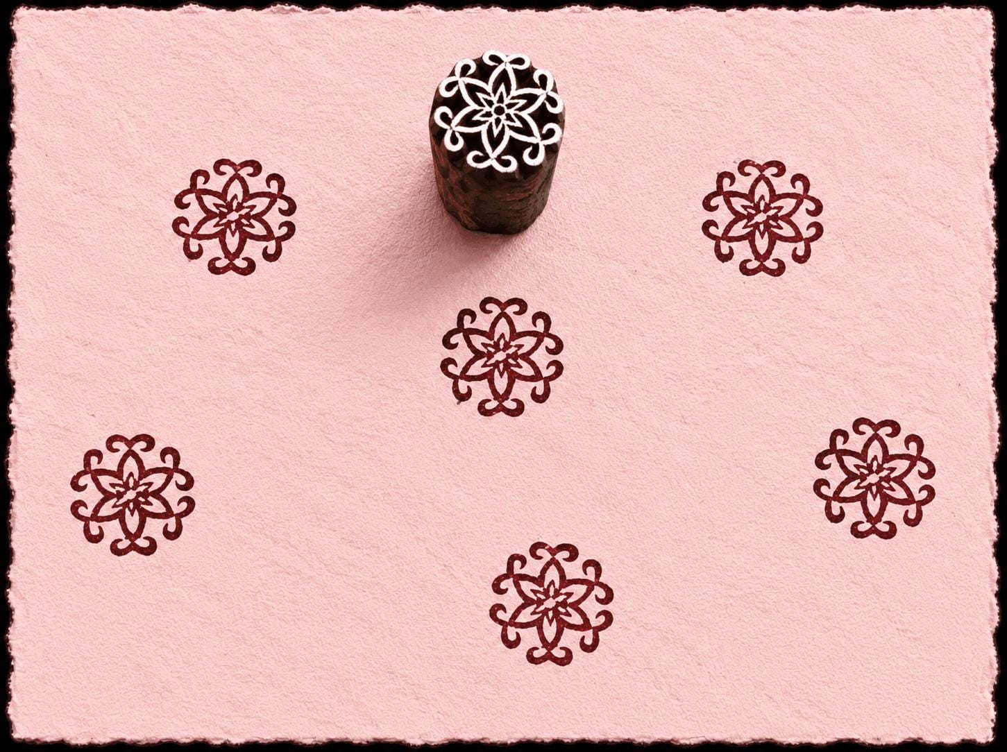 Hand-carved wooden printing block featuring an ornamental Mughal-inspired blossom motif stamped in burgundy ink on pale pink handmade paper.