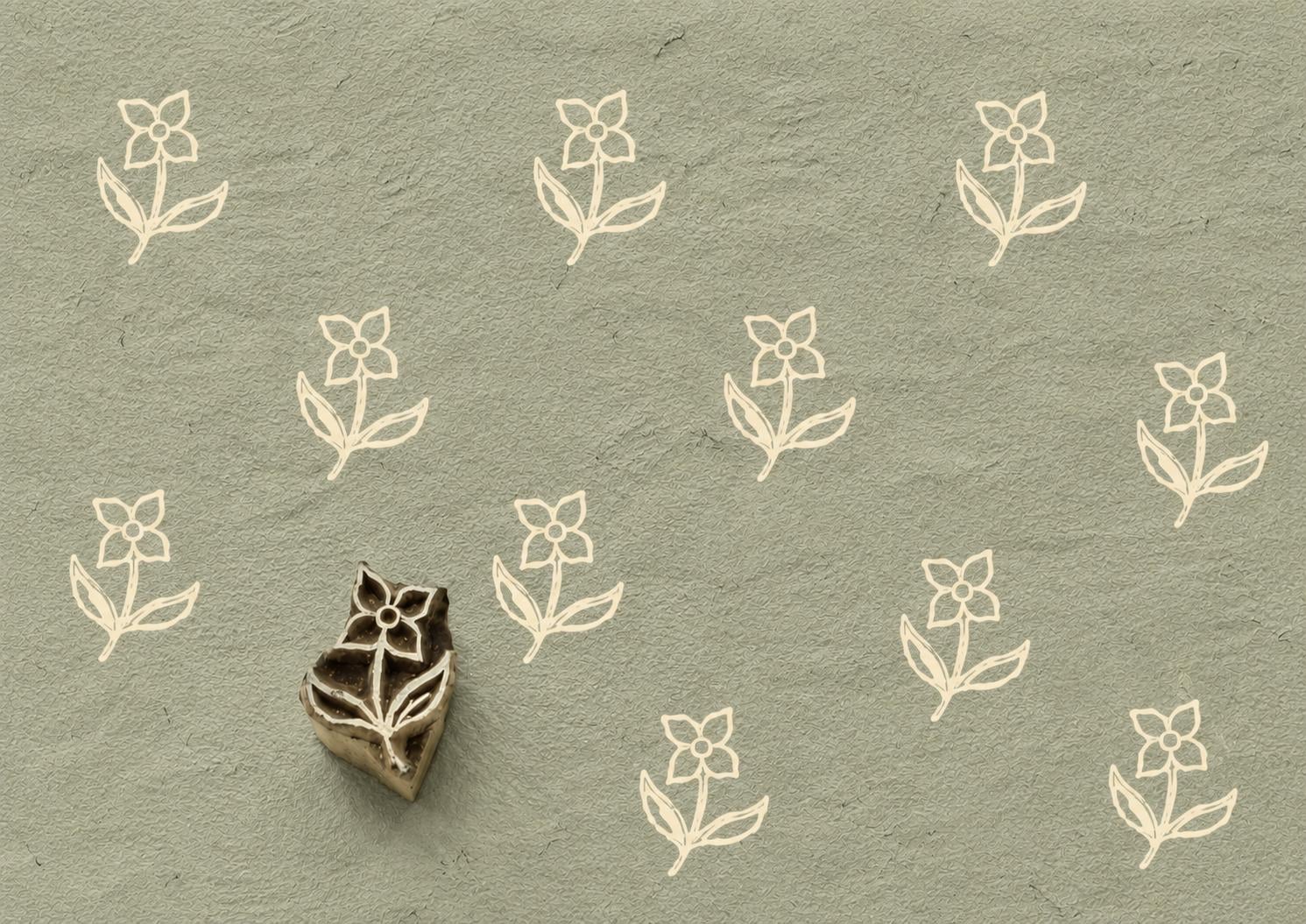 Hand carved Indian wooden printing block featuring a simple folk wildflower motif stamped on sage green handmade paper, ideal for fabric printing, pottery decoration, clay work, and paper crafts.