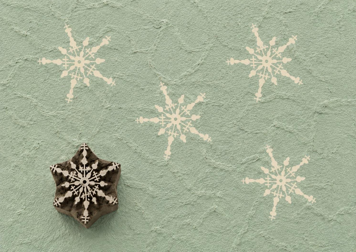 Hand carved wooden printing block featuring an intricate snowflake design stamped on handmade paper, suitable for holiday fabric printing, gift wrap, pottery, clay, and winter craft projects.
