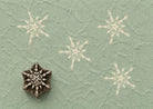 Hand carved wooden printing block featuring an intricate snowflake design stamped on handmade paper, suitable for holiday fabric printing, gift wrap, pottery, clay, and winter craft projects.