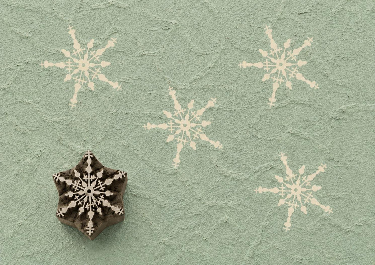 Hand carved wooden printing block featuring an intricate snowflake design stamped on handmade paper, suitable for holiday fabric printing, gift wrap, pottery, clay, and winter craft projects.