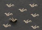 Hand-carved wooden printing block featuring a simple folk bird motif stamped repeatedly in ivory ink on textured charcoal handmade paper.