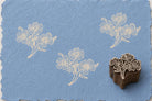 Hand-carved wooden printing block featuring a wildflower bouquet design stamped in ivory ink on textured blue handmade paper.