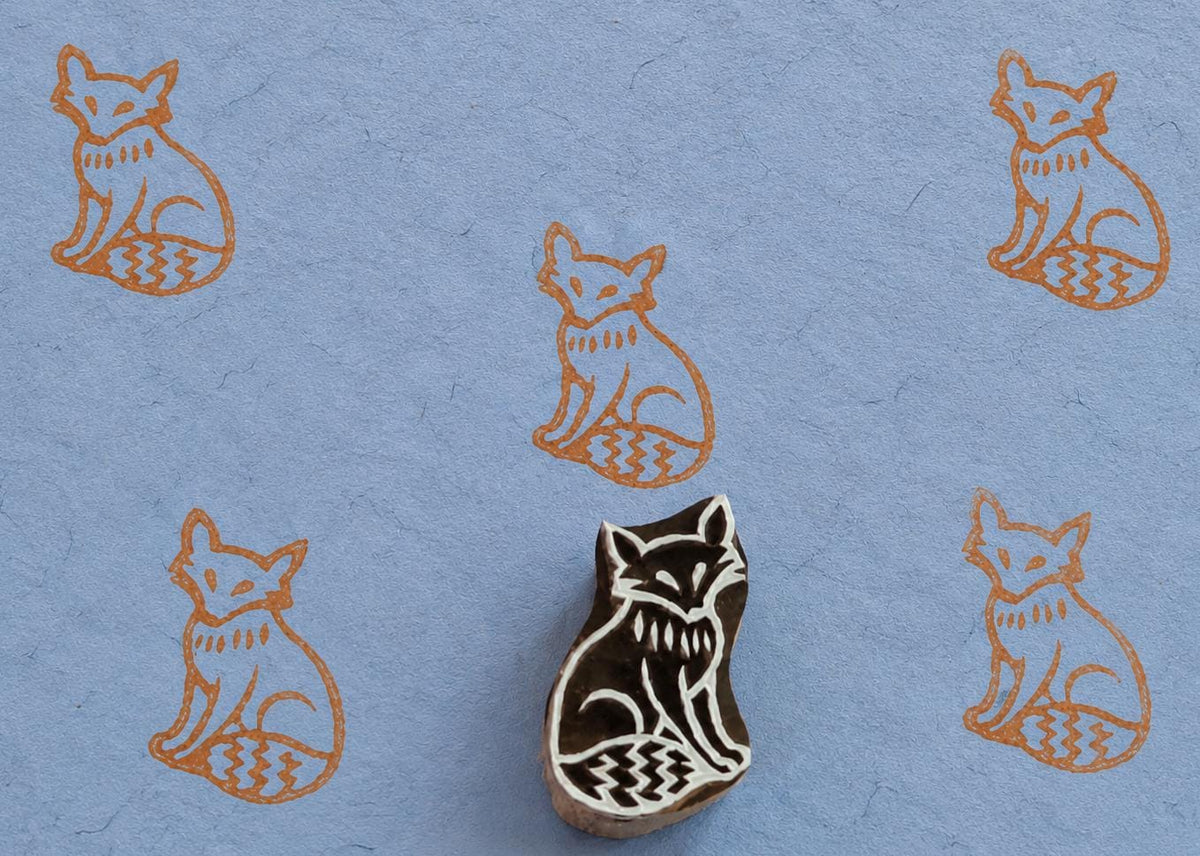 Hand carved Indian wooden printing block featuring a Nordic-style fox with a geometric patterned tail, stamped in copper ink on handmade blue paper, suitable for fabric printing, pottery decoration, clay impressions, and paper crafts.