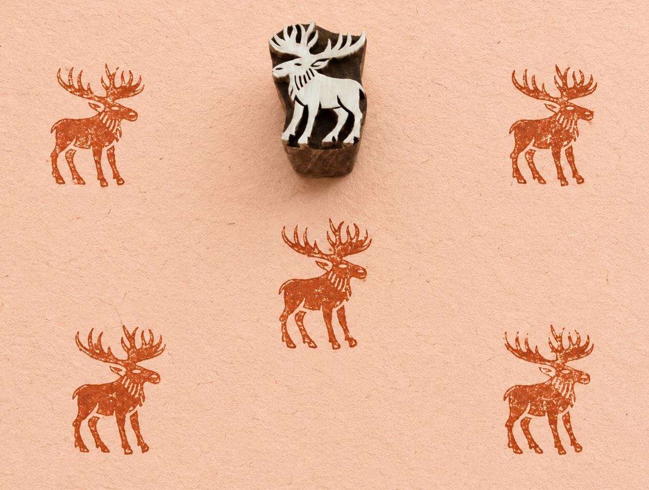 Hand carved moose printing block with repeated wildlife impressions on artisan paper.
