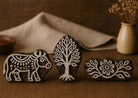 Hand carved wooden printing block set featuring a folk cow, sacred tree, and floral border design arranged together on a rustic wooden surface.