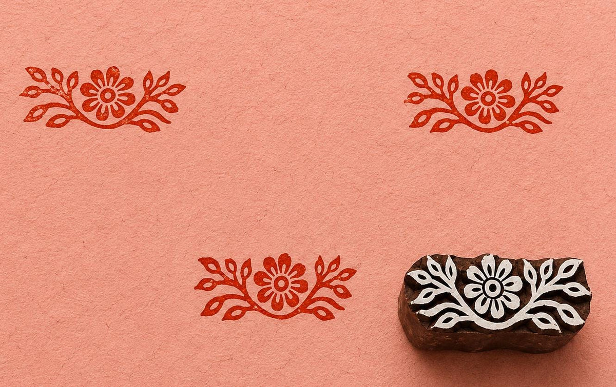 Hand carved wooden printing block featuring a floral border design with red stamped impressions on textured handmade paper.