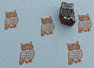 Hand-carved wooden printing block featuring a barn owl design with large decorative eyes and patterned feathers, stamped in brown ink on handmade blue paper.