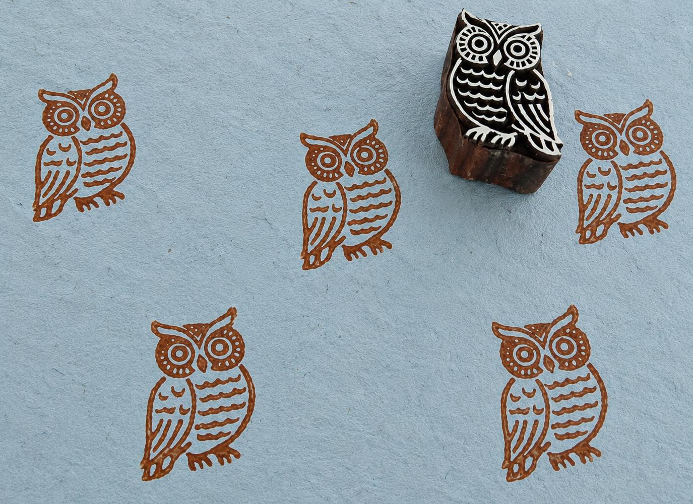 Hand-carved barn owl wooden printing block shown with repeated owl impressions on handmade blue paper.