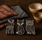 Three hand-carved wooden printing blocks featuring a deer, fox, and owl displayed together on a rustic wooden surface with folded textiles in the background.
